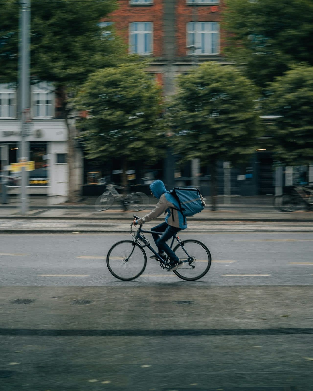 Repartidor en bicicleta con mochila de reparto, andando por una calle de la ciudad