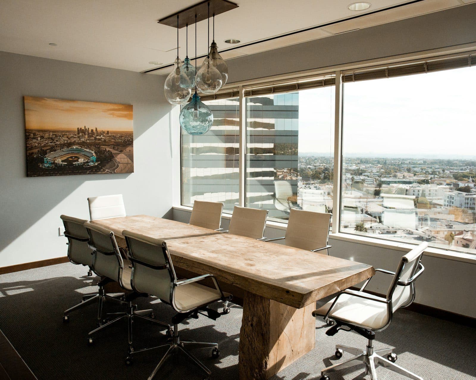 Sala de reuniones vacía con una mesa de madera y sillas, vista de ciudad de fondo